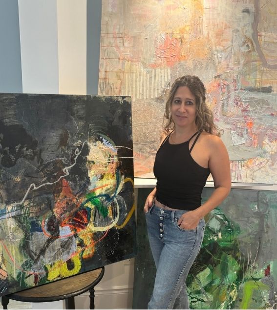 Sari Zon standing beside her paintings in her studio